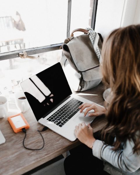 girl wearing grey long-sleeved shirt using MacBook Pro on brown wooden table