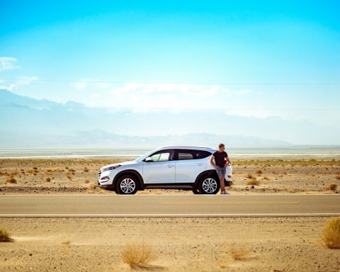 man standing beside white SUV near concrete road under blue sky at daytime