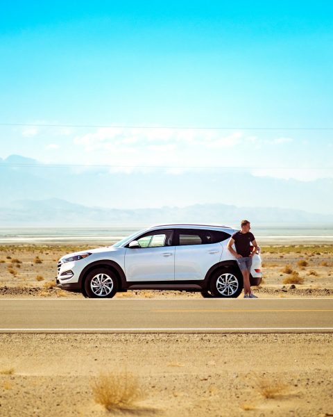 man standing beside white SUV near concrete road under blue sky at daytime