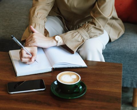 Vrouwelijke ondernemer aan bureau met notitieboek en laptop, nadenken over nieuwe strategie