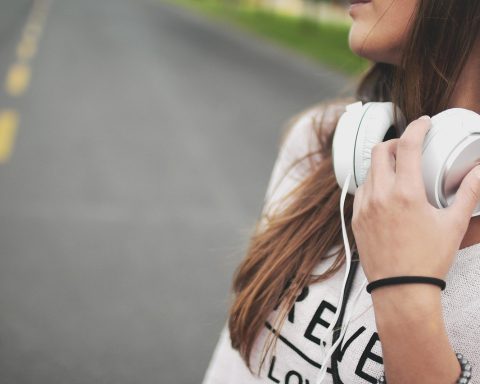Vrouw luistert naar podcast met koptelefoon terwijl ze aantekeningen maakt in een notitieboek