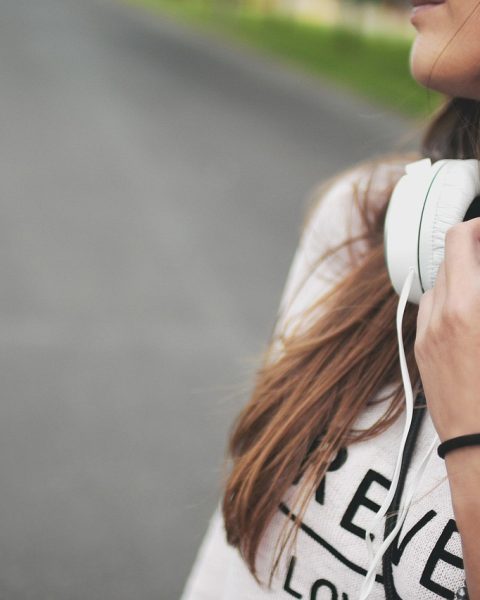 Vrouw luistert naar podcast met koptelefoon terwijl ze aantekeningen maakt in een notitieboek