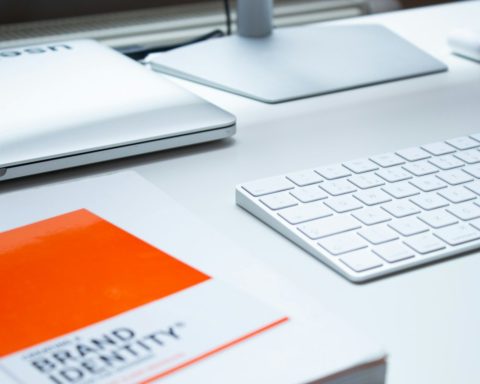A white keyboard, laptop, and book on a clean desk in a workspace