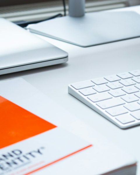 A white keyboard, laptop, and book on a clean desk in a workspace