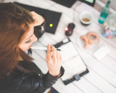 Vrouwelijke ondernemer die nadenkend achter haar bureau zit met een notitieboekje voor zich