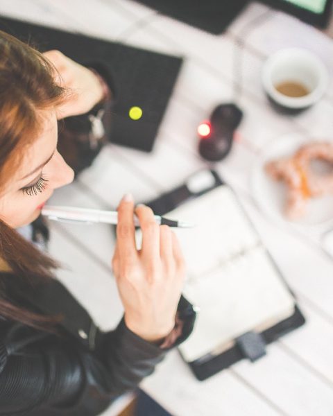 Vrouwelijke ondernemer die nadenkend achter haar bureau zit met een notitieboekje voor zich